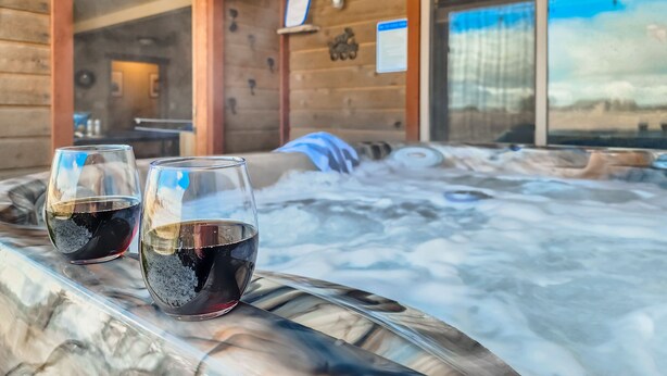 A wooden cabin interior with a hot tub and two glasses of red wine on a marble surface. - Spacious Cabin with Hot Tub, Fire Pit, Game Room (Island Park,)
