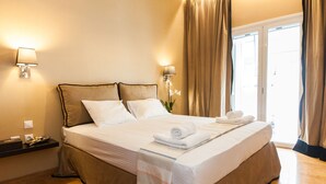 A neatly made bed with white linens, two bedside lamps, and a view of the outdoors through a window with curtains. - Upscale Kolonaki Experience Elegant Apt (Athens)