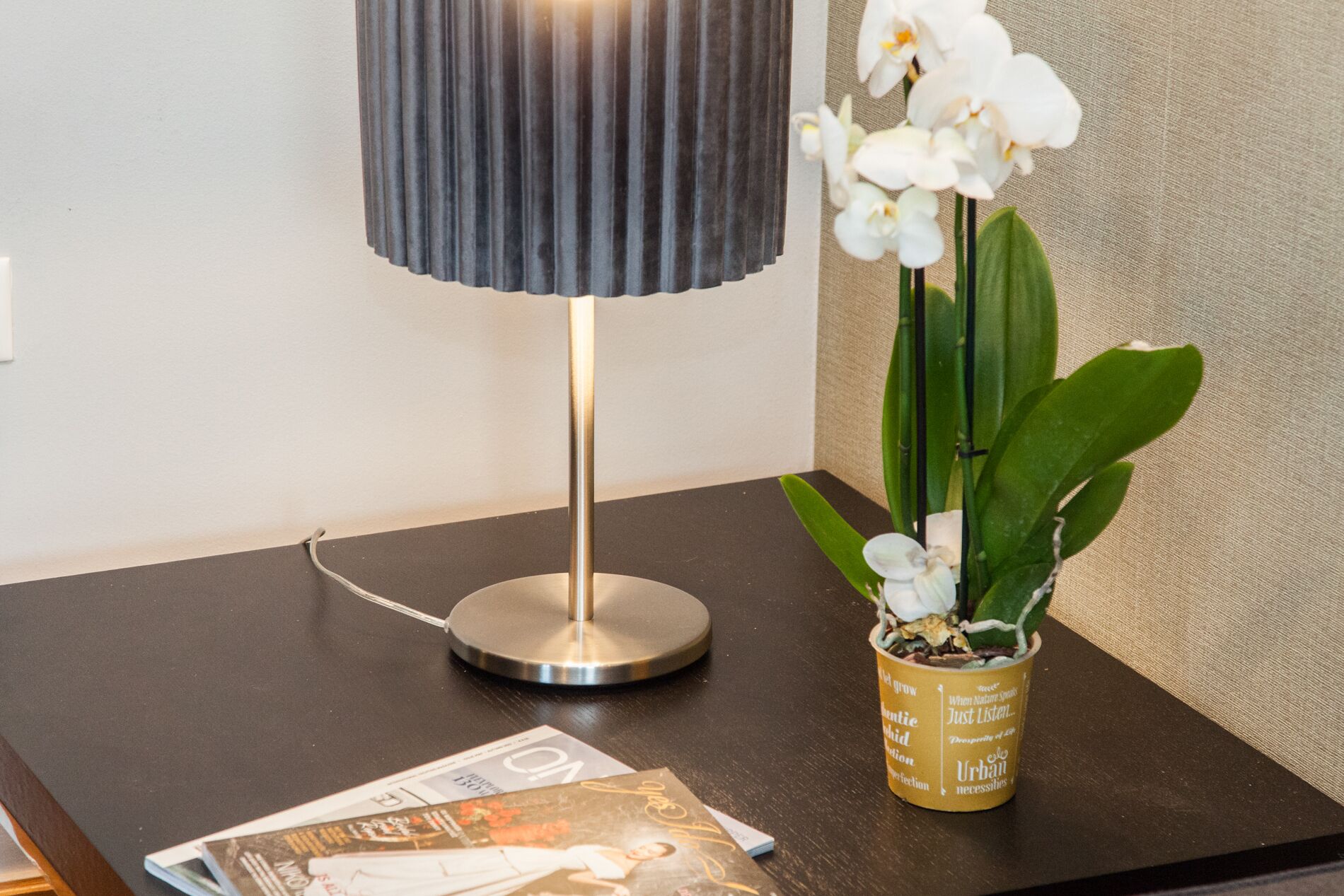 A table with a lamp, an orchid plant, and a magazine.