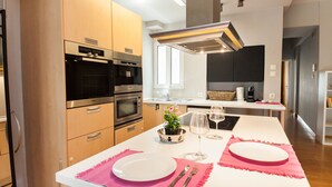 A modern kitchen with built-in appliances, a dining area with pink placemats, and a view into the living space. - Upscale Kolonaki Experience Elegant Apt (Athens)