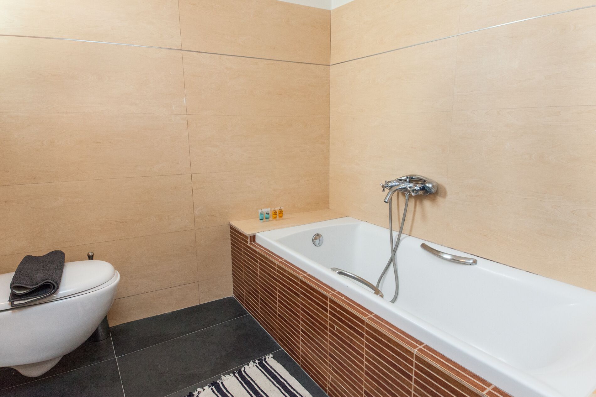 A modern bathroom with a white toilet, a bathtub with a showerhead, and a small shelf with toiletries.