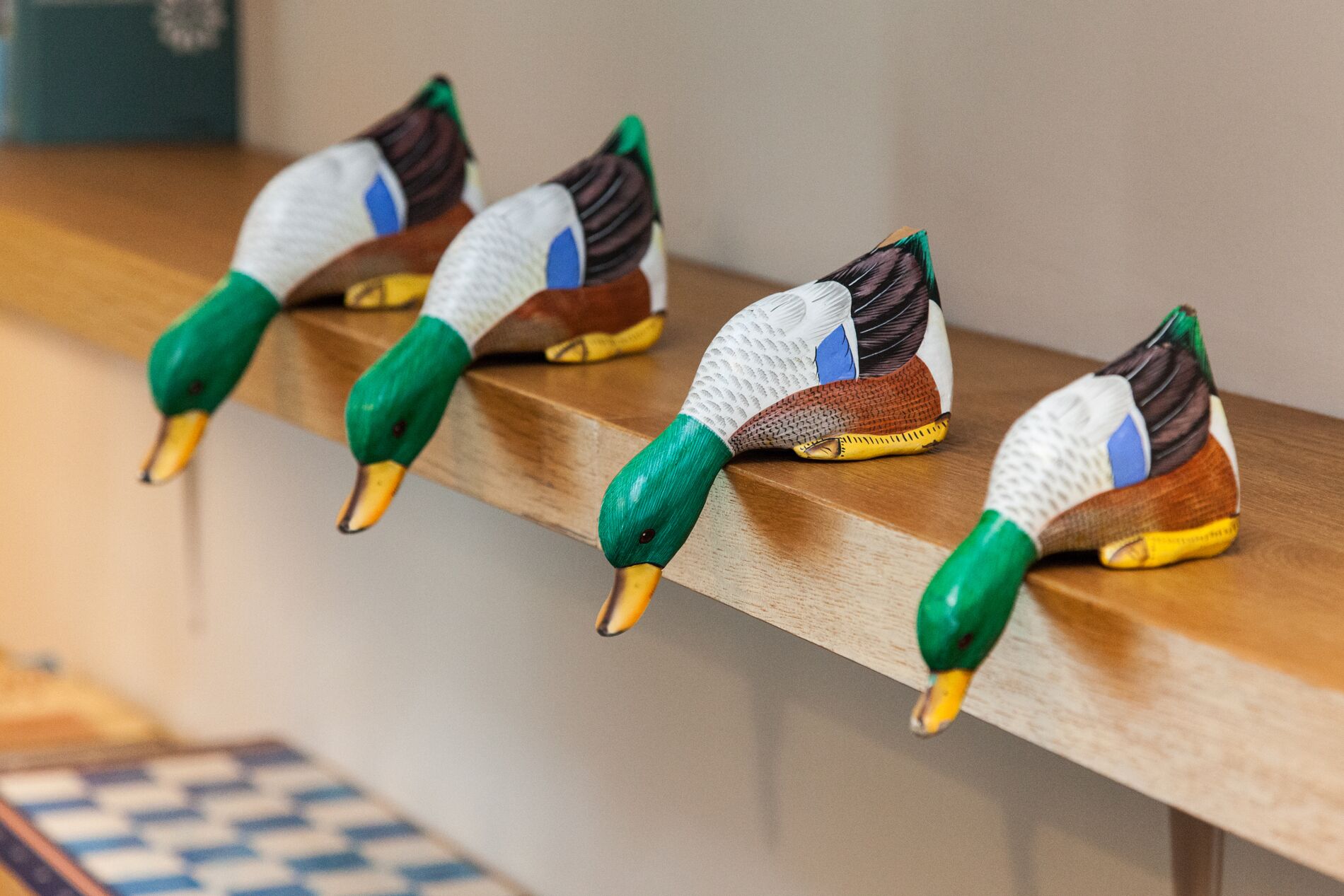 Quatre décorations en forme de canard, posées sur une étagère en bois.