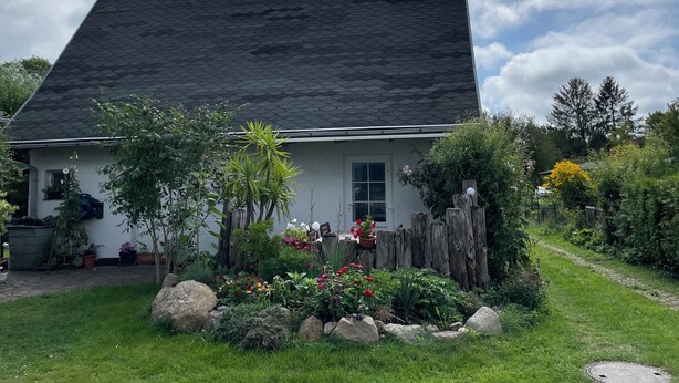 Una casa dal tetto scuro, circondata da un giardino ricco di piante e fiori.