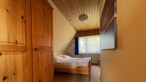 Una camera da letto con un'armadio in legno, un letto, una finestra vista e un soffitto spiovente.