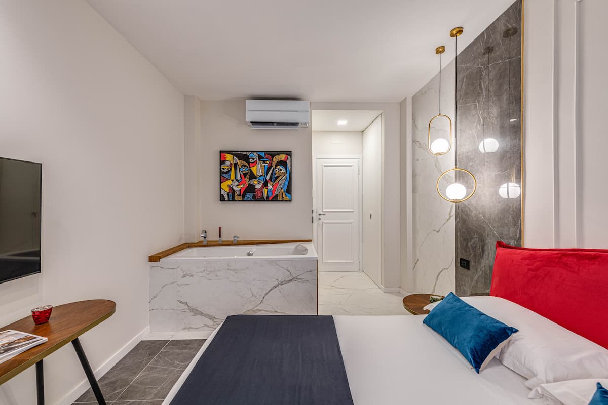 Een moderne slaapkamer met een groot bed, een nachtkastje, een televisie, een badkamer met bad en een marmeren wand.