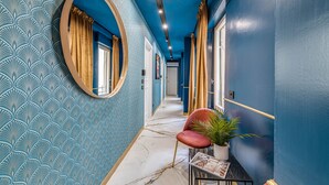 A hallway with a patterned wallpaper, a round mirror, a red chair, and a potted plant. - 7heaven pontevecchio rooms (Florence)