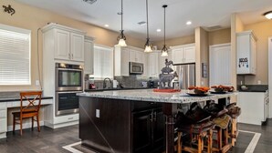 A spacious kitchen with white cabinets, a large island with stools, and modern appliances. - Welcome to Paradise | Pool Table, Swim Up Bar, Htd Pool, Hot Tub, Casita! (Mesa)