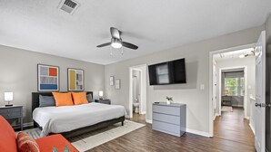 A modern bedroom with a large bed, a ceiling fan, a flat-screen TV, and a walk-in closet.
