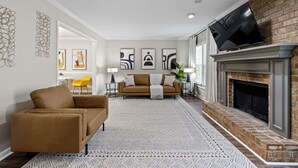A living room with a brown sofa, a fireplace, and a TV mounted above it.