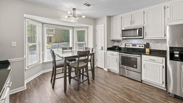 A modern kitchen with white cabinetry, stainless steel appliances, and a dining area with a wooden table and chairs.