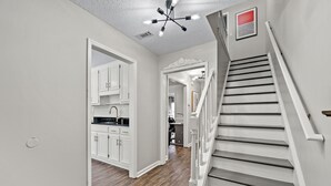 A hallway with a staircase, white walls, and wooden flooring.