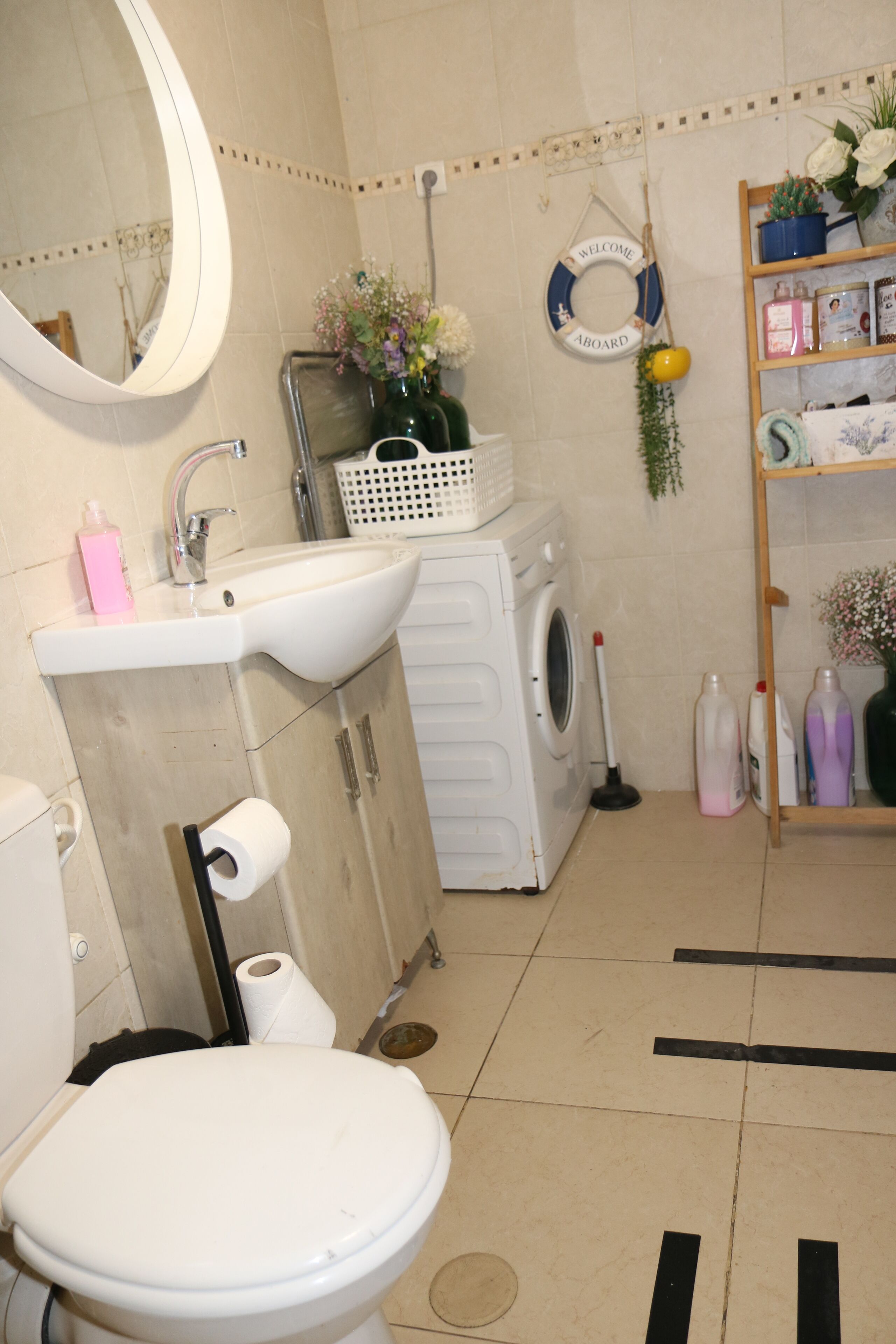 Une salle de bain équipée de toilettes, d’un lavabo, d’un lave-linge et d’une étagère où sont rangés les articles de toilette.