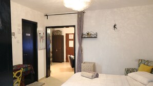 A bedroom with a bed, a chair, a table with a tablecloth, and a door leading to another room. - The private house Beer Sheba (Beersheba)