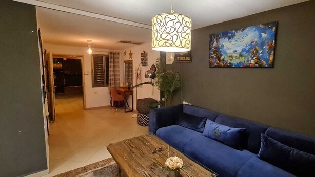 A living room with a blue sofa, a wooden coffee table, a hanging lamp, and a painting on the wall. - The private house Beer Sheba (Beersheba)