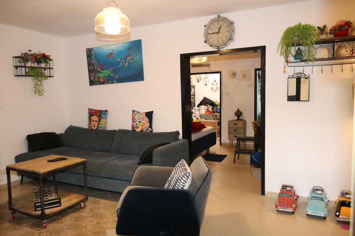 Una sala de estar con un sofá, una mesa de centro, una mesita con una planta, un cuadro, un reloj y coches de juguete.