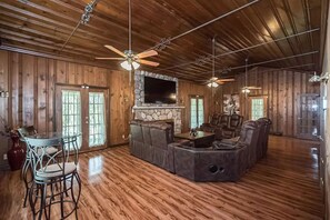 A spacious living room with wooden floors, a stone fireplace, leather sofas, and a ceiling fan. - Retreat Home, Swimming Pool, jacuzzi, sauna, Game room, Basketball Court . (St. Louis)
