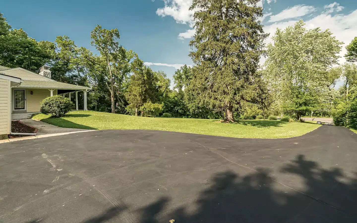 A residential driveway leading to a house with a covered porch, surrounded by mature trees and a well-maintained lawn.