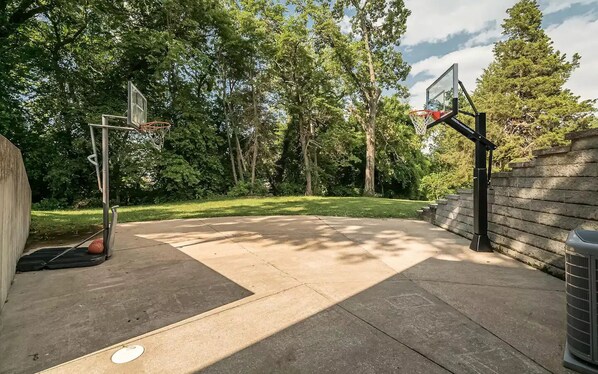 An outdoor basketball court with two hoops, surrounded by trees and a stone wall. - Retreat Home, Swimming Pool, jacuzzi, sauna, Game room, Basketball Court . (St. Louis)