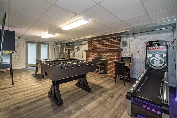 A room with a foosball table, a brick fireplace, and a claw machine.