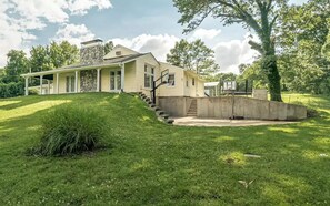 A two-story house with a covered porch, a stone chimney, and a concrete retaining wall.