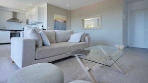 A modern living room with a glass coffee table, a sofa, and a kitchen in the background. - Bright & Modern apartment 300m to the beach, tennis court and pools in Marbella (Marbella)