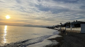 A beach with a row of houses along the shore, a calm sea, and a setting sun. - Bright & Modern apartment 300m to the beach, tennis court and pools in Marbella (Marbella)