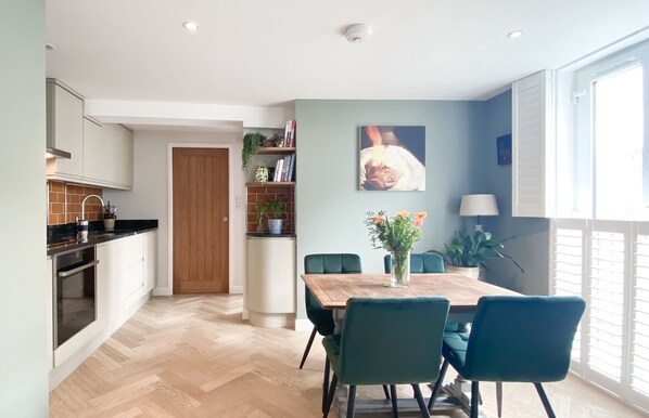 Una cocina moderna con puerta de madera, zona de comedor con mesa y sillas, y vistas al exterior a través de amplios ventanales.