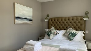 A neatly made bed with white linens and a beige textured blanket, flanked by two green leaf-patterned pillows. - The Old Stables - Luxury Dartmouth town centre apartment w/ parking permit (Dartmouth)
