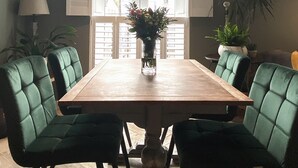 A dining room with a wooden table, green upholstered chairs, and a vase with flowers. - The Old Stables - Luxury Dartmouth town centre apartment w/ parking permit (Dartmouth)