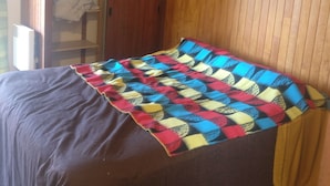 Ein Schlafzimmer mit einem Bett, das mit einem farbenfrohen Patchwork überzogen ist, einem Holzschrank und einem Regal mit einem Bild.
