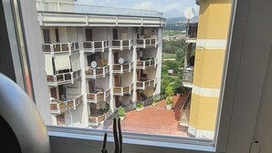 A window view of a residential building with balconies, a potted cactus, and a woven basket with a bottle. - La Mansarda Suite (Benevento)