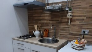 A compact kitchen with a gas stove, a sink, a small refrigerator, and a wooden backsplash. - La Mansarda Suite (Benevento)