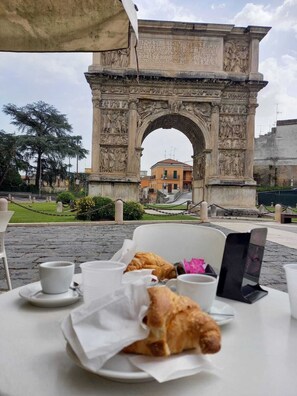 Una mesa con un croissant y una taza, frente a un antiguo arco con detalles tallados.