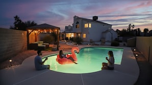A swimming pool with a flamingo float, a covered patio, and a house in the background.