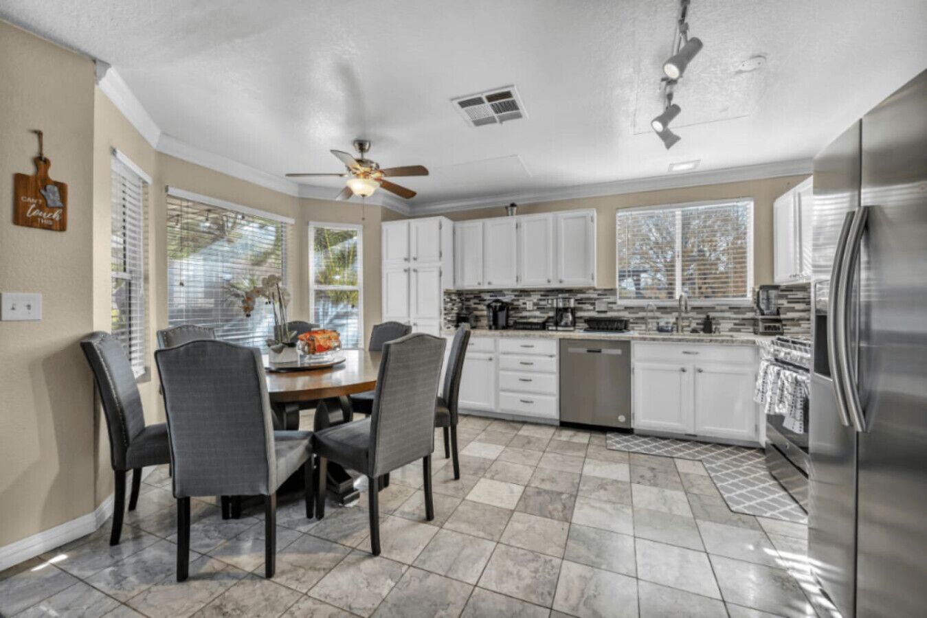 A modern kitchen with white cabinets, a stainless steel refrigerator, and a dining area with a table and chairs.