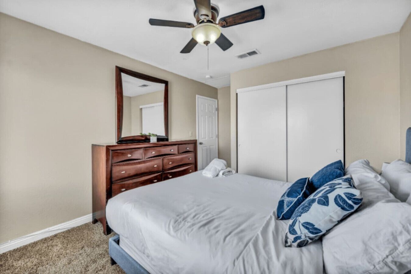 A bedroom with a bed, dresser, mirror, and ceiling fan.