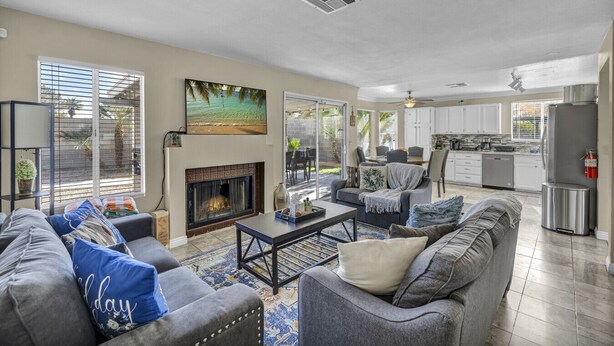 A spacious living area with a fireplace, comfortable seating, a kitchen, and large windows.