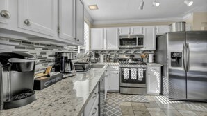 A modern kitchen with white cabinets, stainless steel appliances, a coffee bar, and a patterned floor.