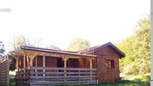 Un rustico chalet in legno con veranda e un fabbricato secondario, immerso nel verde.