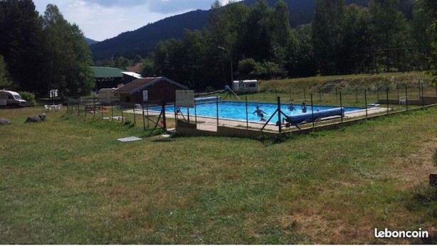 Una piscina circondata da un prato, con un piccolo edificio sullo sfondo e una montagna.