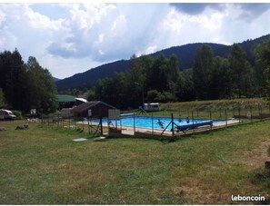 A swimming pool surrounded by a grassy area with a small building and a mountain in the background. - Agréable Chalet Nature Calme (Cornimont)