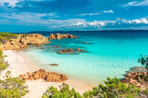 Un paysage côtier caractérisé par une eau turquoise et limpide, des formations rocheuses et une plage de sable.