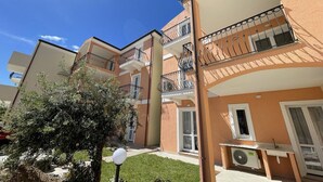 Un immeuble résidentiel à plusieurs étages, doté de balcons, d’un petit espace jardin et d’un appareil de climatisation visible.