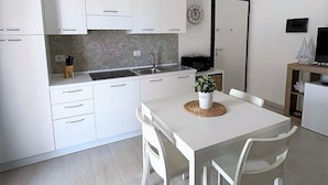 Une cuisine moderne avec des meubles blancs, un îlot central et un coin repas avec des chaises blanches.
