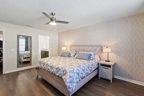 Une chambre à coucher avec un lit, une table de chevet, un ventilateur de plafond et un mur décoré d’un motif.