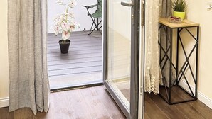 Quarto com porta de vidro deslizante que dá para um pátio externo. Há uma pequena mesa com um vaso de planta e uma cadeira.