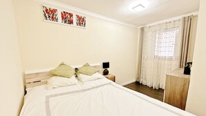 Quarto com cama grande, mesa de cabeceira, luminária e janela com cortinas.