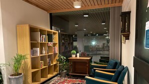 A cozy reading nook with a bookshelf, a blue armchair, a patterned rug, and a small table with a plant. - BORG Sommerhotell (Ålesund)