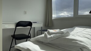 A hotel room with a bed, a desk, a chair, and a window with a view of the sky. - BORG Sommerhotell (Ålesund)