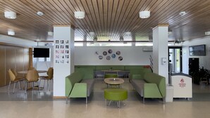 A modern lobby with a wooden ceiling, green seating, a reception desk, and a TV screen. - BORG Sommerhotell (Ålesund)